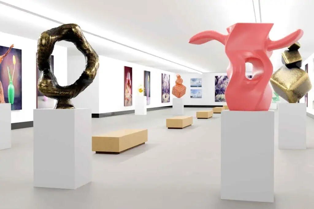Ein Innenraum einer Kunstgalerie mit modernen Skulpturen auf Sockeln und Gemälden an den Wänden, mit Holzbänken in der Mitte des Raumes.