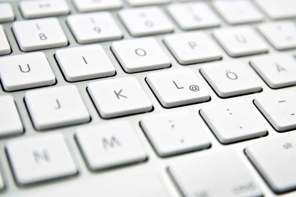 Nahaufnahme einer weißen Computertastatur mit leicht abgerundeten Tasten und deutschen Umlauten wie Ö und Ä.
