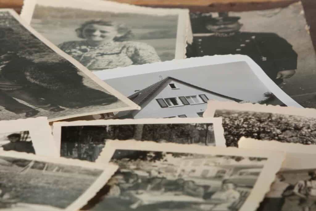 Eine lose Ansammlung alter Schwarz-Weiß-Fotos, darunter Porträts von Personen, ein Haus und Naturaufnahmen, wobei die Ränder der Fotos ungleichmäßig geschnitten sind.