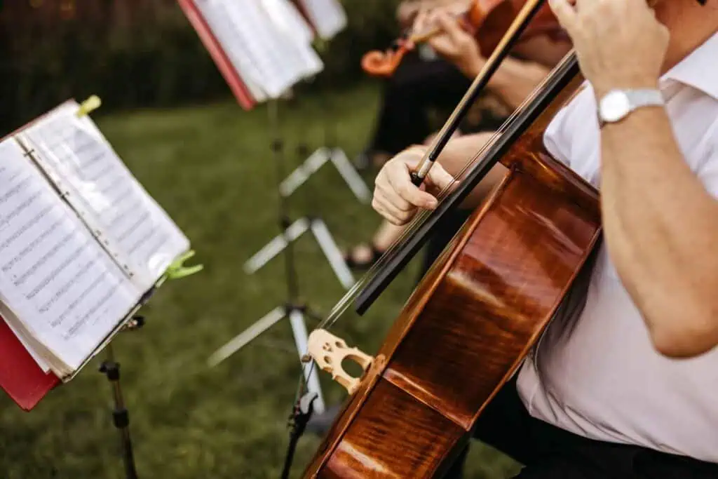 Nahaufnahme einer Person, die ein Cello spielt, mit Notenständern und einer weiteren Musikerin im Hintergrund, die Geige spielt.